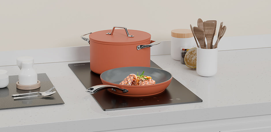 Ceramic cookware set on a stove with food, surrounded by kitchen utensils.