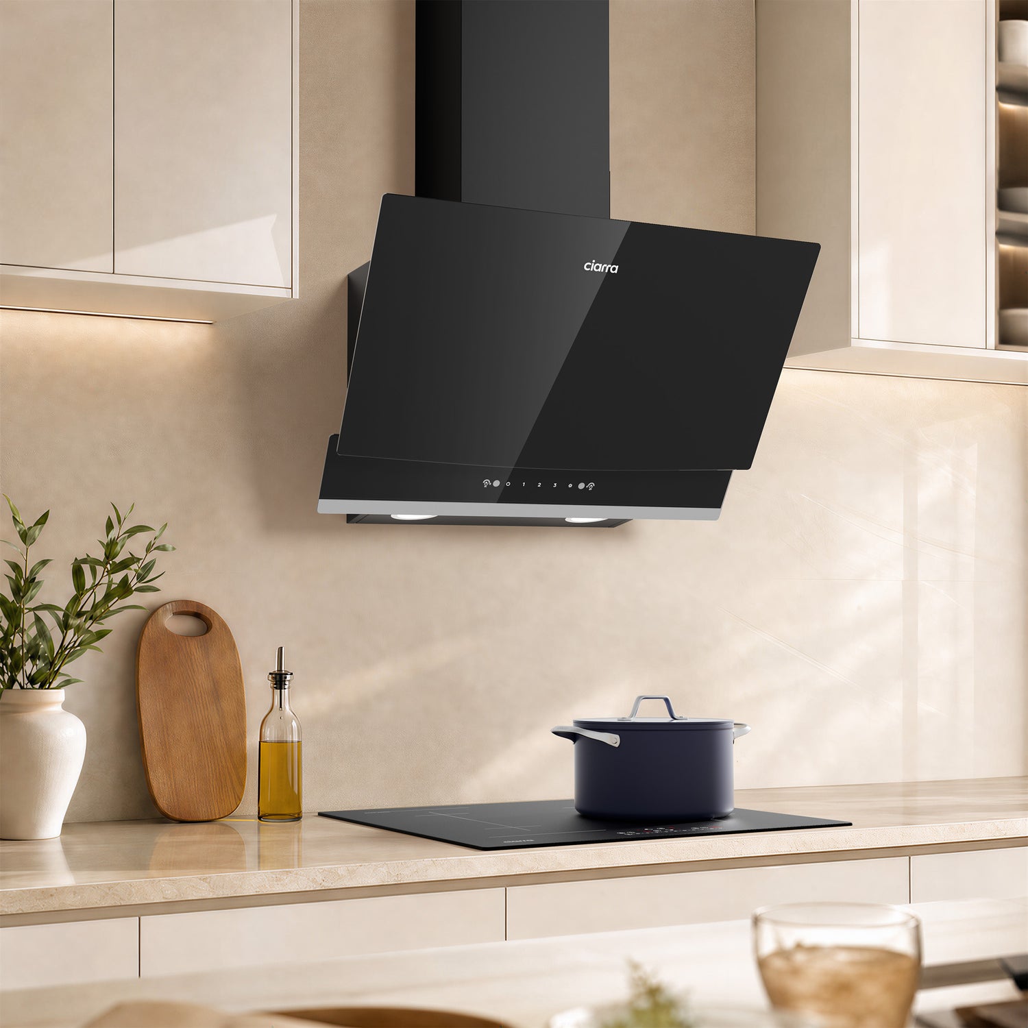 A modern black CIARRA cooker hood mounted on a beige tiled kitchen wall above a built-in cooktop, with kitchen cabinets, a pot, and countertop decor in the background.