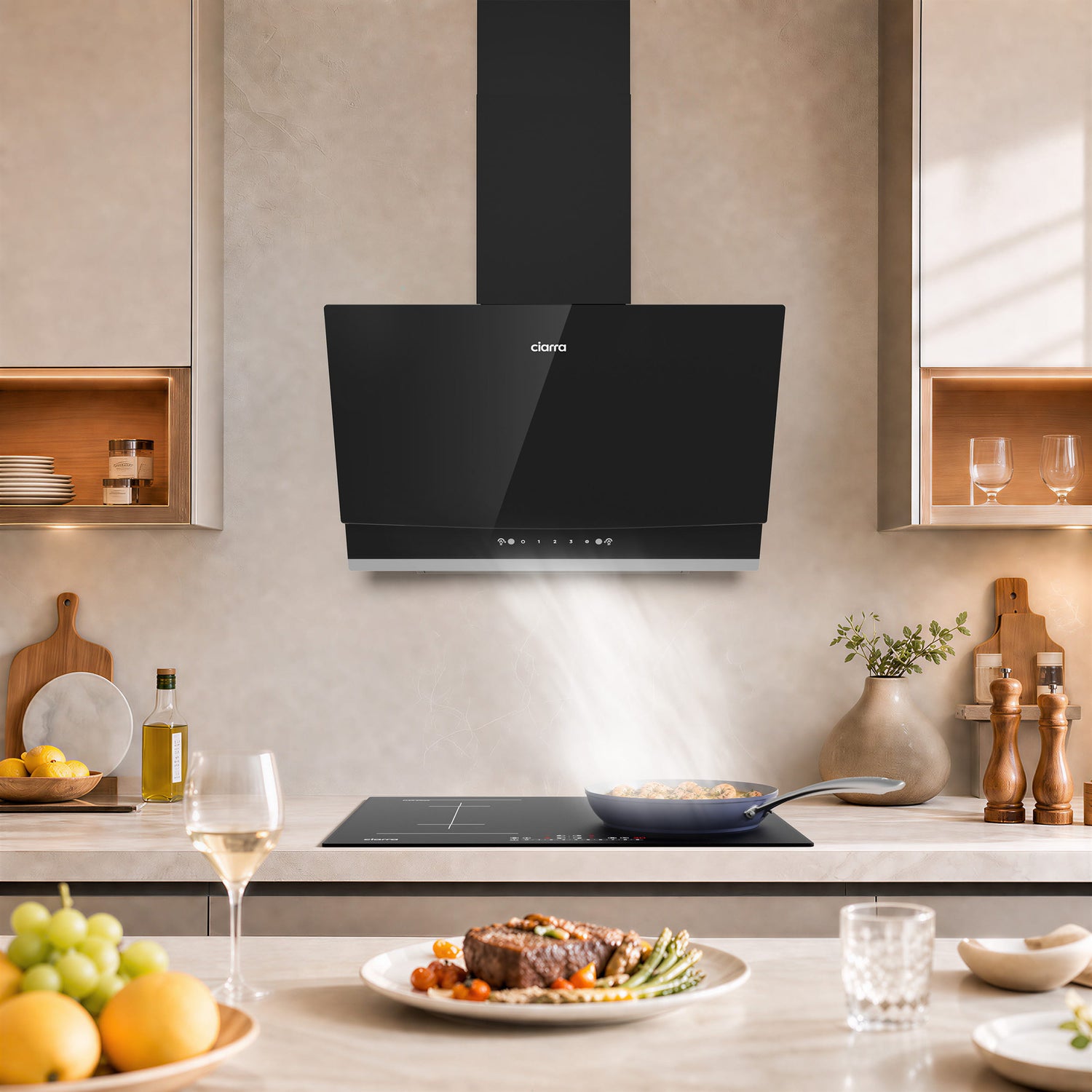 A sleek black CIARRA cooker hood mounted on a beige kitchen wall above a modern cooktop, with a plated steak, wine glass, and fruit in a well-lit contemporary kitchen.