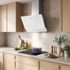 A white CIARRA cooker hood mounted on a light stone backsplash above a black induction cooktop in a modern kitchen with light wood cabinets and countertop decor.