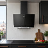 A black CIARRA cooker hood mounted on a light grey textured wall in a modern kitchen setting with dark cabinets, a window view, and kitchen props on the counter.
