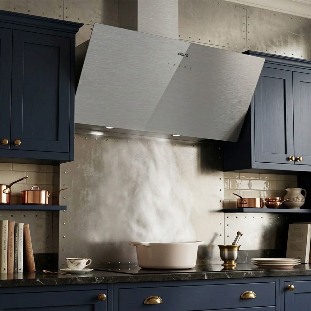 Ciarra 90cm brushed glass slanted cooker hood capturing cooking vapors over an induction cooktop.